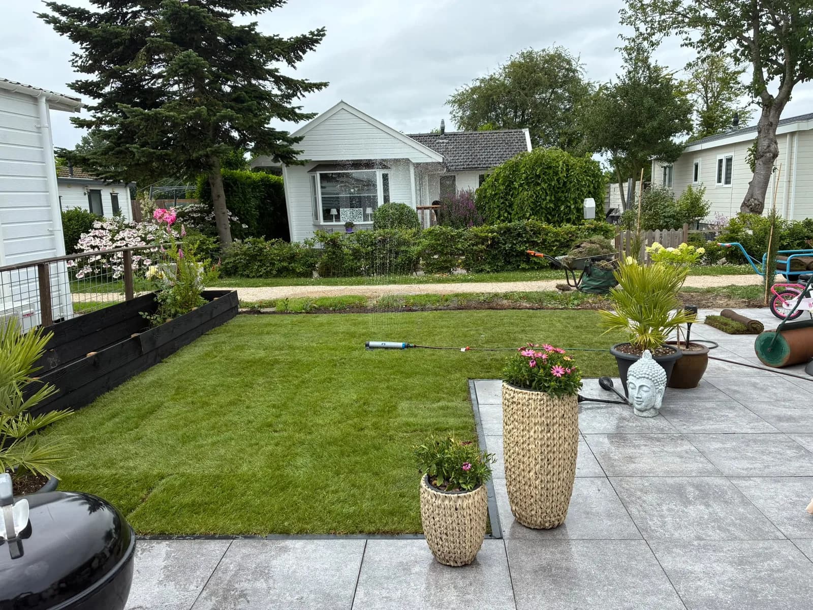 Vers aangelegd gazon naast een terras met plantenbakken
